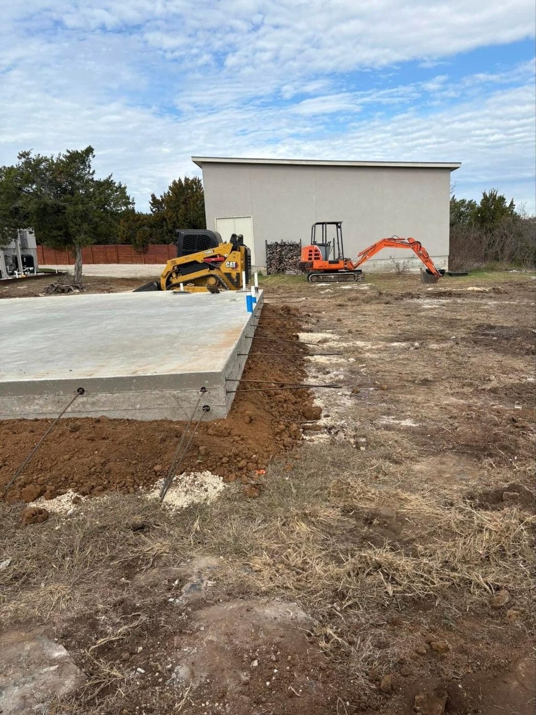 Concrete slab with a track loader and mini excavator beside a building