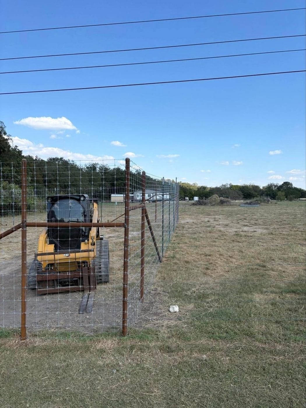 Track loader inside a new wire fence on pipe posts